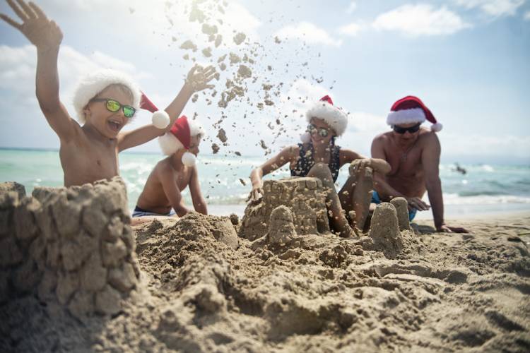family playing on beach, all wearing Santa hats